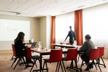 3 collaborateurs travaillant dans une salle de séminaire, avec un vidéoprojecteur et des tables dressées en format U